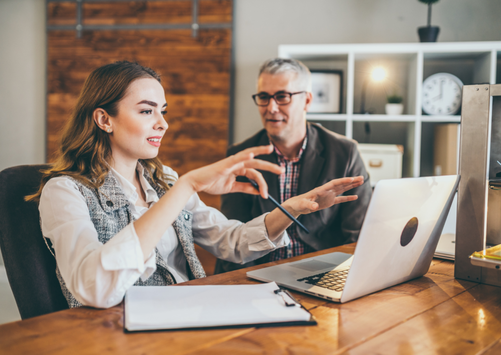 Doi profesioniști discutând un plan de acțiune la laptop, ilustrând importanța sprijinului într-o sesiune de mentorat și coaching